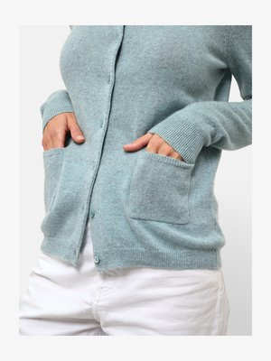 Lichtblauwe cardigan van zacht materiaal, met een knoopsluiting aan de voorkant, geribbelde manchetten en twee voorzakken. De textuur lijkt glad te zijn.