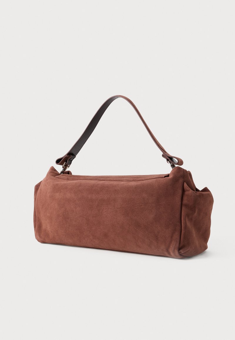 Bolso de ante marrón con forma rectangular redondeada. Cuenta con un asa de cuero y un cierre de cremallera en la parte superior. Textura suave y diseño estilizado.