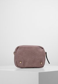 Pieni suorakaiteen muotoinen laukku, joka on valmistettu syvänvioletista kuvioidusta nahasta. Siinä on kultaiset metalliosat, vetoketjusuljin ja lyhyt musta hihna.