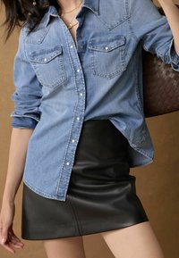 Denim-Hemd mit langen Ärmeln und Druckknopf-Taschen, kombiniert mit einem schwarzen Leder-Minirock. Es zeichnet sich durch einen lässigen Schnitt und eine leichte Textur aus.