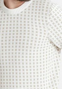 Pletený svetr v off-white barvě, s texturovaným mřížkovým vzorem a žebrovaným kruhovým výstřihem. Látka má měkký a prodyšný vzhled.