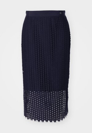 Tengerészkék kötött ceruzaszoknya, textúrált mintával, bordás derékpánttal és háromszög alakú kivágásokkal díszített szegéllyel.