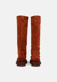 Paire de bottes hautes en daim couleur rouille avec talons en bois empilés, vues de dos sur un fond blanc.