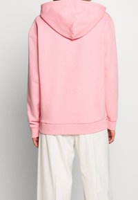 Sweat à capuche en coton rose avec capuche, poignets côtelés et ourlet. Texture lisse et coupe décontractée. Porte avec un pantalon léger et ample.