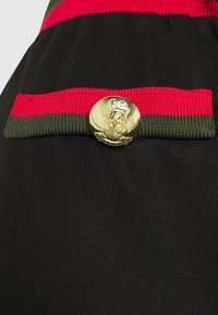 Svart tyg med en strukturerad yta har ett rött och grönt rand och en guldkknapp med en präglad lejonemblem.