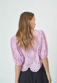 Lilac, puff-sleeve blouse with eyelet cutouts and scalloped hem. Fabric appears lightweight with a textured finish. Back view shown.