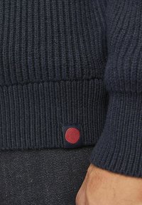 Navy gestreifter Pullover mit strukturiertem Strick, der am Saum ein markantes gesticktes Patch eines roten Kreises auf navy Hintergrund hat.