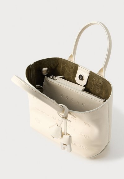 Κρεμ δερμάτινη τσάντα με δομημένο σχήμα, εσωτερικό από πράσινο σουέτ, λαβές στο επάνω μέρος και ανάγλυφο λογότυπο· περιλαμβάνει μια μικρή τσαντούλα με φερμουάρ στο εσωτερικό.