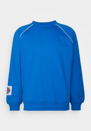 Blue sweatshirt with a round neckline, ribbed cuffs, and hem. Features white piping along the shoulders and a logo patch on the sleeve.