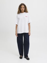 White oversized t-shirt featuring red "SOURDOUGH" text, paired with dark blue wide-leg jeans and black slip-on shoes.