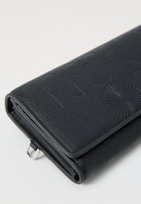 Portefeuille en cuir noir avec des motifs en relief, incluant des cercles et des formes d'éventail. Il a une texture lisse et un détail en métal.