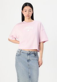 Rosa cropped t-skjorte med korte ermer, med hvit tekst "CONVERSE ALL STAR" og stjernelogo. Brukt med et høyt liv denimskjørt.