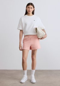 T-shirt blanc oversize, short rose avec taille élastique, baskets blanches et sac de couleur crème. Textures lisses, design simple et couleurs neutres.