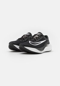 Baskets de sport noires avec une tige en mesh, une bande d'accent blanche, un bout rond et une semelle intermédiaire blanche épaisse. Semelle extérieure en caoutchouc noir texturé.