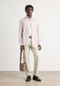 Camicia a righe bianca e rossa, pantaloni beige, scarpe nere e una borsa a tracolla marrone chiaro.