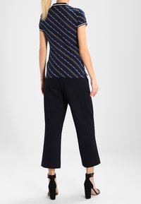 T-shirt blu con strisce diagonali bianche e verdi, maniche corte e colletto nero, abbinato a pantaloni cropped blu e tacchi neri.