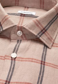 Chemise beige à carreaux avec des rayures rouges et noires, deux boutons blancs fermés, et une étiquette de la marque Seidensticker à l’intérieur du col.