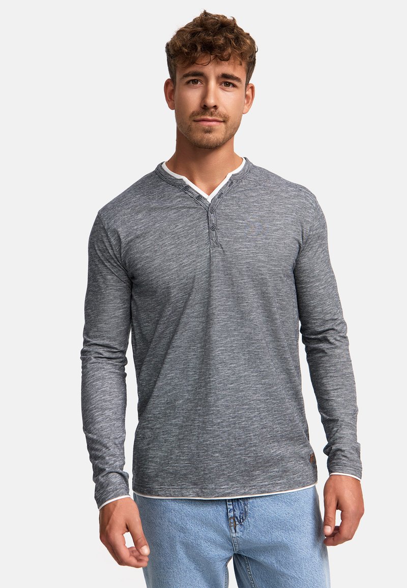 Camisa henley de manga larga gris con una tela texturizada, con una abertura de dos botones, detalle de cuello blanco y mangas ajustadas. Llevada con jeans de color azul claro.