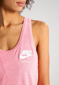 Rosa Nike linne med texturerad tyg, djupa ärmhål och en vit logotyp med "JUST DO IT" tryckt nedanför.