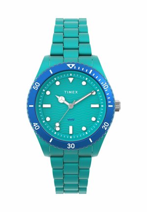 Montre Timex turquoise avec un cadran à motif de vague, une lunette bleue et un bracelet en acier inoxydable. Index et aiguilles blancs pour une meilleure visibilité.