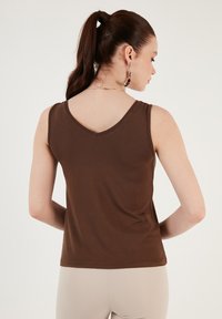Brown sleeveless top with a V-neck design, made from soft fabric. The back features a smooth texture and clean stitching details.