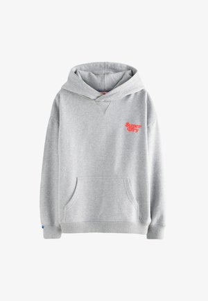 Ung dreng med rødt hår iført en lysegrå Superdry hættetrøje og beige bukser, stående mod en neutral baggrund.