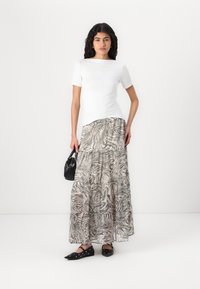 Fehér, rövidujjú felső, amelyet egy laza, több szintből álló, fekete-fehér mintás maxi szoknyával párosítanak. A modell egy kis fekete kézitáskát tart és lapos cipőt visel.