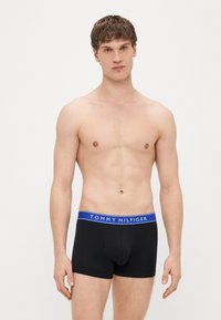 Cuecas boxer de algodão pretas com uma cós azul apresentando o logotipo branco "TOMMY HILFIGER", ajuste justo e comprimento até o meio da coxa.