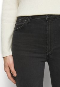Jeans de denim negro de tiro alto con una textura suave, que cuentan con un bolsillo frontal y un cierre de botón, combinados con un suéter de canalé claro.