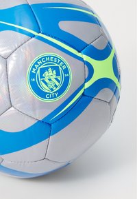 Pallone da calcio con pannelli blu, verde chiaro e argento che presenta il logo del Manchester City e l'anno di fondazione 1894 su sfondo bianco.