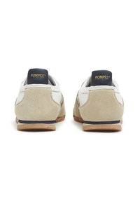Sneakers with a white leather upper and beige suede accents, featuring a navy heel tab with gold lettering and a rubber sole.
