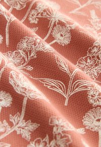 Tissu à texture douce de couleur corail atténuée avec de délicats dessins floraux blancs en lignes et des plis subtils mettant en valeur le motif tissé.