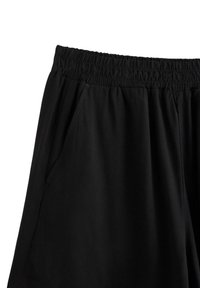 Sorte sportsshorts med elastisk talje og sidelommer. Stoffet er glat og let, designet til komfort og bevægelighed.