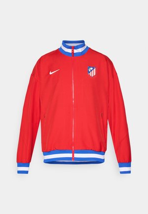 Rød sportjakke med lynlås, blå og hvide stribede manchetter og kant, med et Nike-logo og klubemblem på venstre bryst.