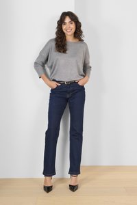 Grå strikket sweater, mørkeblå jeans, sorte højhælede sko. Sweateren har en bred neckline og løs pasform; jeansene er lige ben med subtil syning.