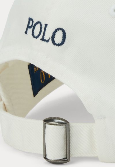 Belega trakca za baseball kapo z metalno zaponko in vezenim napisom "POLO" v temno modri barvi na zadnji strani kape.