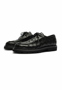 Un paio di scarpe nere in pelle con lacci, caratterizzate da un motivo intrecciato e suole in gomma spessa, su sfondo bianco.