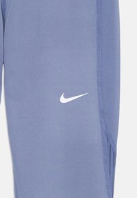 Svetlomodré športové legíny s hladkou textúrou, s bielym logom Nike na dolnej ľavej strane a kontrastnými švami.