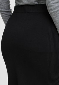 Melnā ribotā svārku ar gludu tekstūru, ar piegulīgu jostu un vertikālām krokām vienā pusē, apvienota ar pelēku ilgu piedurkņu topu.