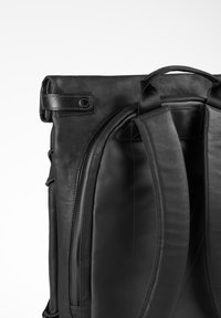 Schwarzer Lederrucksack mit gepolsterten Schultergurten, einem Tragegriff oben und einer gerollten Klappe, die mit einem Druckknopf gesichert ist.