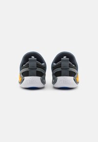 Zapatos Nike con una parte superior de color azul oscuro, acentos grises y detalles en amarillo brillante en el talón. Presentan una lengüeta reforzada en el talón y una plantilla acolchada.