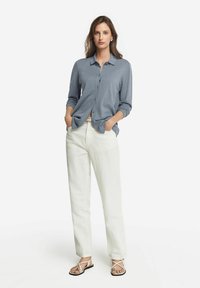 Lätt, långärmad skjorta med knappar i mjukt blått. Matchad med vita, avslappnade byxor och flata sandaler med remmar.