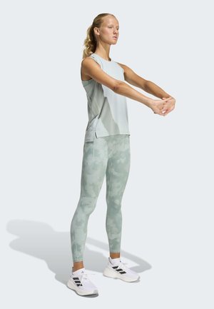 Camiseta sin mangas deportiva de color verde claro y leggings con estampado de camuflaje. Diseño ajustado con textura suave. Zapatillas blancas con detalles en negro completan el conjunto.