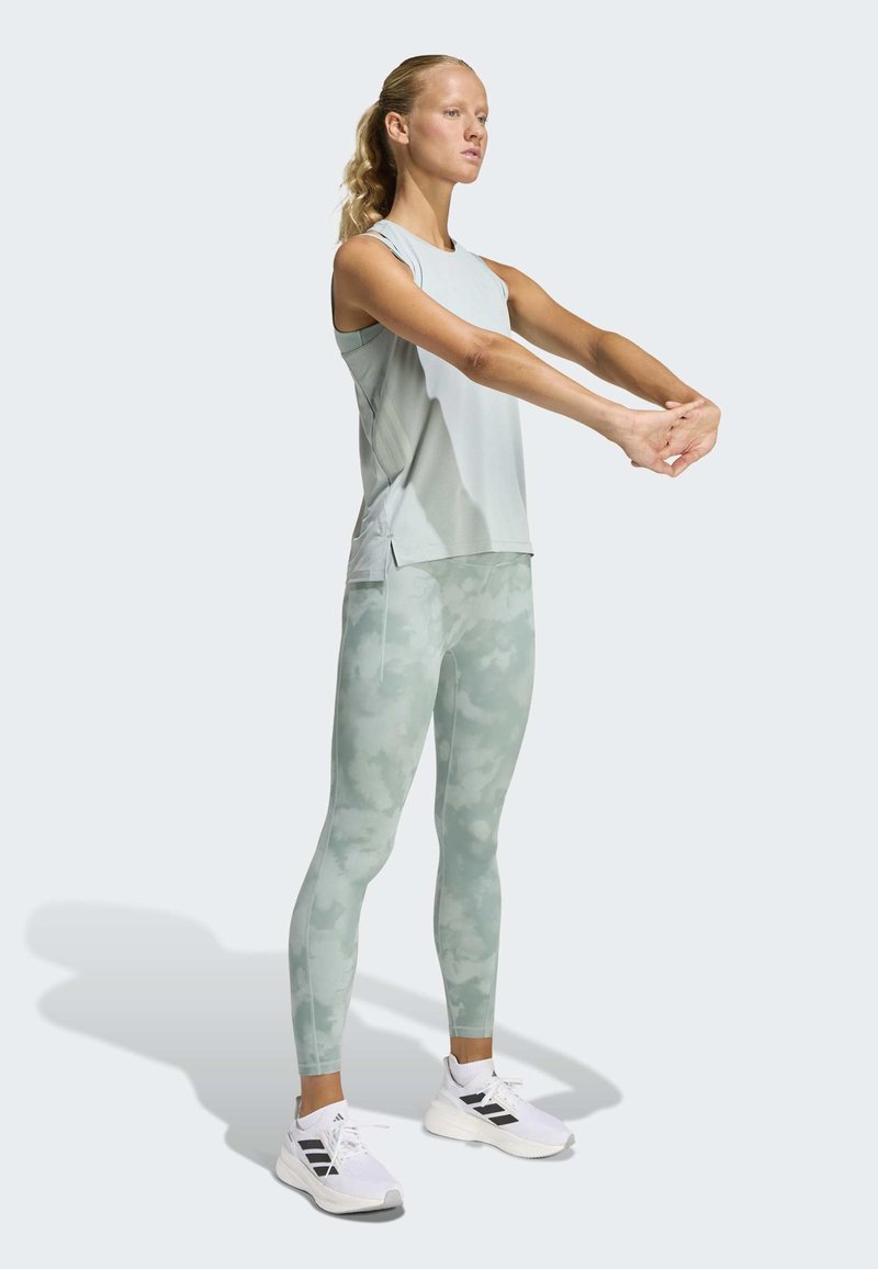 Αθλητικό τοπ σε ανοιχτό πράσινο και κολάν καμουφλάζ. Εφαρμοστό σχέδιο με λείο υλικό. Το σύνολο ολοκληρώνουν λευκά αθλητικά παπούτσια με μαύρες λεπτομέρειες.