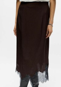 Schwarzer Midi-Rock mit gewelltem Saum und Spitze, getragen mit einem weißen Oberteil und schwarzen Stiefeln, die Hände und ein Handgelenksarmband zeigend.