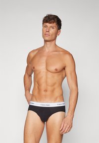 Schwarze Baumwollunterhosen mit einem weißen elastischen Bund, der mit dem "Calvin Klein"-Logo versehen ist, entworfen für Komfort und Unterstützung.
