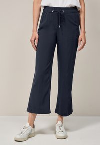 Pantalons bleu marine à coupe décontractée avec une taille élastique et un cordon de serrage, jambes légèrement évasées, assortis à des baskets blanches.