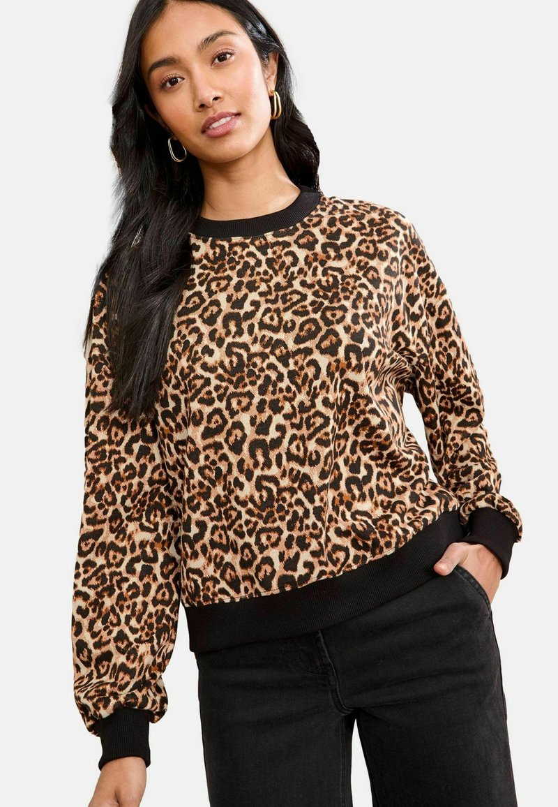 Leopardų rašto džemperis su minkšta medžiaga, juodu gubu apykakle ir rankovėmis, bei laisvai krentančiu kirpimu. Derinamas su juodomis kelnėmis.