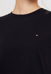 Černé bavlněné tričko s kulatým výstřihem a krátkými rukávy. Na hrudi se nachází malé vyšívané logo v červené, bílé a modré barvě.