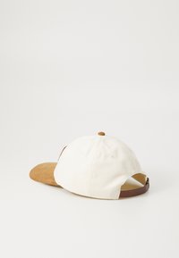 Balta beisbola cepure ar brūnu zamšādas vizieri un brūnu regulējamu siksnu. Aprīkota ar mazu apaļu pogu augšā un ventilācijas atverēm.
